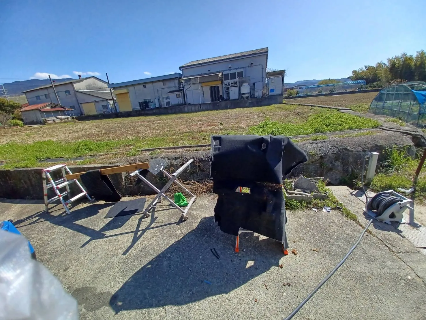 車から取り外した黒いフロアカーペットを屋外の台に掛けた状態